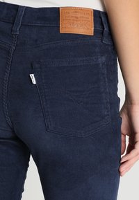 Pantalon en velours côtelé bleu marine à surface texturée, avec un patch en cuir portant l'inscription "Levi Strauss & Co." et une poche arrière avec un détail de couture.