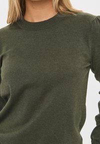 Olivgrön stickad tröja med ribbad rund halsringning och texturerat tyg. Passformen är något avslappnad med subtila detaljer på axlarna.