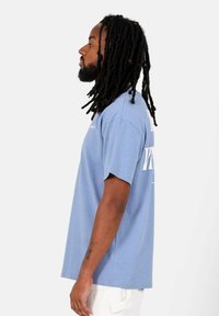 Lichtblauwe t-shirt met korte mouwen en een relaxte pasvorm, met een witte bedrukte tekstontwerp op de achterkant en een zachte, gladde textuur.