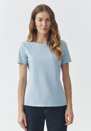 Light blue short-sleeve top made from smooth fabric, featuring a round neckline and a fitted silhouette. Worn with dark denim jeans.
