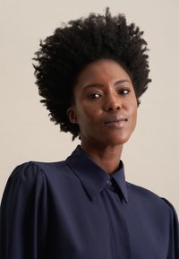 Blusa navy con collo strutturato e chiusura con bottoni, dotata di maniche a sbuffo e texture di tessuto liscia. Design semplice ed elegante.