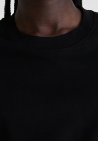 Black cotton t-shirt featuring a ribbed crew neckline and smooth texture. The fabric appears soft and fitted around the collar area.