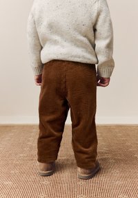 Hnedé manžestrové nohavice voľného strihu s vertikálnymi rebrami, v kombinácii s béžovými mäkkými čižmami a svetlosivým svetríkom s bodkami.