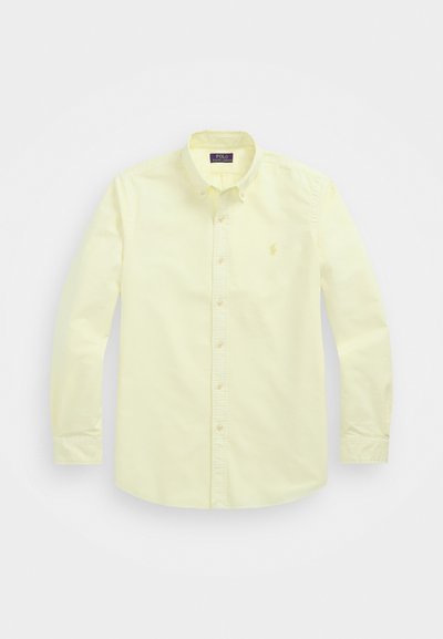 Svetložltá košeľa na gombíky so širokým golierom, dlhými rukávmi a malým vyšitým logom na ľavej hrudi. Bavlnený materiál, hladká textúra.