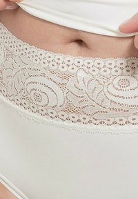 Lingerie bianca con pizzo e decorazioni floreali, presenta bordi ondulati. Tessuto morbido sopra la vita, che mette in risalto i delicati dettagli in pizzo.