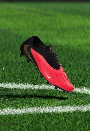 Scarpetta da calcio Nike rossa e nera che fluttua sopra l’erba verde vicino alle linee bianche del campo.