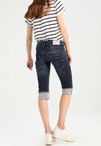 Tummat farkku capri-housut, joissa on käännetyt lahkeet, takataskut ja erivärinen ompelu, yhdistettynä raidalliseen lyhythihaiseen paitaan.