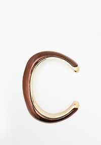 Bracelet métallique brillant en forme de la lettre C, avec une surface extérieure en bronze lisse et une surface intérieure en or poli sur fond blanc.
