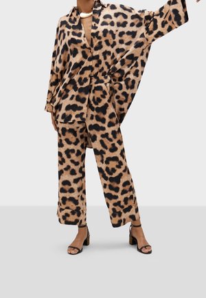 Femme portant un haut ample à imprimé léopard avec de larges manches et un pantalon court assorti, associé à des sandales à talons noires et un collier en or.