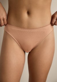 Světle růžové žebrované bikiny s elastickým páskem a jemnou krajkovou výšivkou. Měkká textura, střih s mírně zvýšeným pasem a plným krytím na zadní straně.