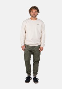 Sudadera crema con puños acanalados, combinada con pantalones cargo verdes que cuentan con bolsillos laterales y puños elásticos. Unas zapatillas negras completan el look.