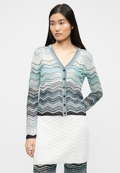 Διαφανής ζακέτα με μακριά μανίκια και V-λαιμόκοψη, με ζιγκ-ζαγκ σχέδιο σε διάφορες αποχρώσεις του μπλε και μαύρου, καθώς και σκουρόχρωμα κουμπιά.