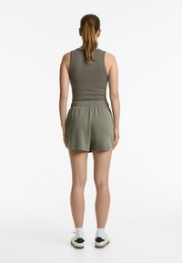 Débardeur en olive côtelé et shorts assortis avec une taille élastique. Les shorts sont à mi-cuisse, en tissu doux, associés à des baskets blanches.