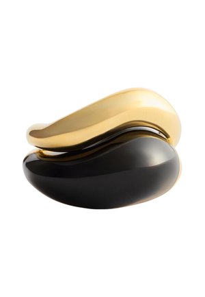 Deux objets lisses, incurvés et en forme de haricot empilés ; l'un en or poli au-dessus, l'autre noir brillant en dessous, sur un fond blanc.