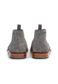 Par de botas de tobillo de ante gris con tacones de madera apilados en marrón y tiradores, mostradas desde la parte trasera sobre un fondo blanco.