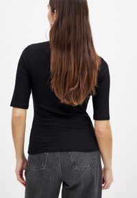 Melna ribota blūze ar trīs ceturtdaļu piedurknēm, ar pieguļošu dizainu un gludu tekstūru, apvienota ar augsta vidukļa pelēkiem biksēm.