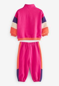 Survêtement pour enfants de couleur rose vif avec des blocs de couleurs orange, bleu marine et crème sur les manches et les côtés du pantalon, avec des poignets et une ceinture élastiques.