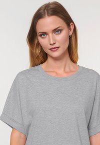 Donna con capelli lunghi e lisci, che indossa una maglietta grigia, posa con sicurezza contro uno sfondo chiaro, mostrando la sua bellezza naturale.
