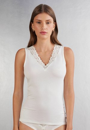 Débardeur blanc en tissu doux, doté d'un décolleté en V profond avec des bordures en dentelle intricée. Texture lisse avec une coupe ajustée, sans motifs.