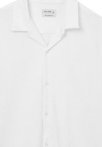 Camicia bianca a maniche corte con vestibilità rilassata, dotata di colletto, texture morbida e cinque bottoni sul davanti.