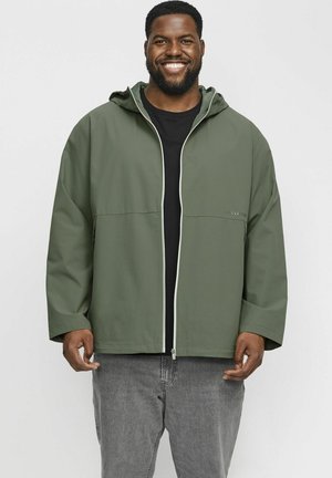 Chaqueta ligera verde oliva con capucha, cremallera frontal y ribetes blancos en contraste. Cuenta con dos bolsillos laterales y un corte relajado.