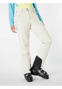 Skibroek in crème met een gestructureerde afwerking, voorzien van zijzakken met rits en een zwarte zoomdetail. Draagt een paar zwarte skischuilen.