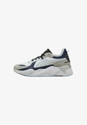 Sneakers Puma con una parte superiore in rete bianca, accenti grigi e blu navy, pannelli testurizzati e una suola spessa bianca con dettagli blu sottili.