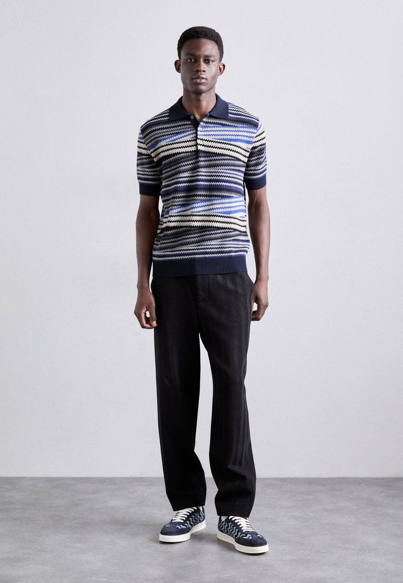 Polo a righe in navy, bianco e blu con maniche corte, abbinato a pantaloni neri texture e sneakers con motivo.