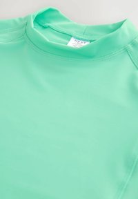 Rövid ujjas, mentazöld fürdőruha felső, sima, könnyű anyagból készült, lapos varrásokkal és magas, kerek nyakkivágással a kényelem és a támasz érdekében.
