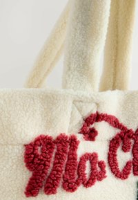 Tote taske i uldblandinger i off-white med blødt rødt broderet tekst. Blød tekstur og kraftige hanke for en behagelig bæring.