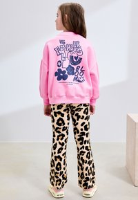 Pink sweatshirt med blomstergrafik på ryggen; kombineret med beige viddebukser med sort leopardmønster. Afslappet fodtøj synligt.