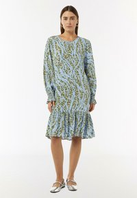 Langermige jurk met een blauw-groen abstract patroon, een gerimpelde zoom en een ronde halslijn, gemaakt van lichtgewicht stof. Zilveren platte schoenen.