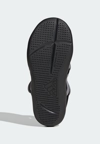 Svart gummisula med texturerad yta, som har cirkulära perforeringar och ett distinkt mönster. Adidas-logotyp synlig.