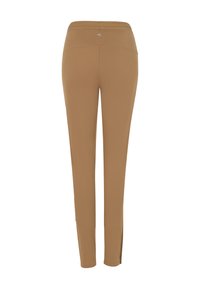 Bruine, aansluitende sportbroek met een gladde textuur, voorzien van uitsparingen bij de enkel en een logo nabij de tailleband.