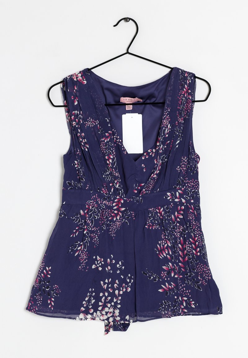 Námořnický květinový overálek s hlubokým výstřihem do V, skládanou tkaninou, krátkou délkou a detailem zavázání na spodním lemu. Zobrazuje růžové a zelené květinové vzory.