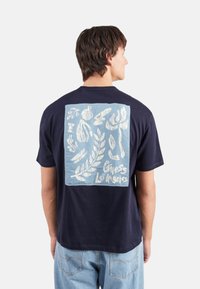 Camiseta de algodón de color azul marino con un gráfico cuadrado de color azul claro en la parte posterior, con formas orgánicas blancas y el texto "Guess Los Angeles".