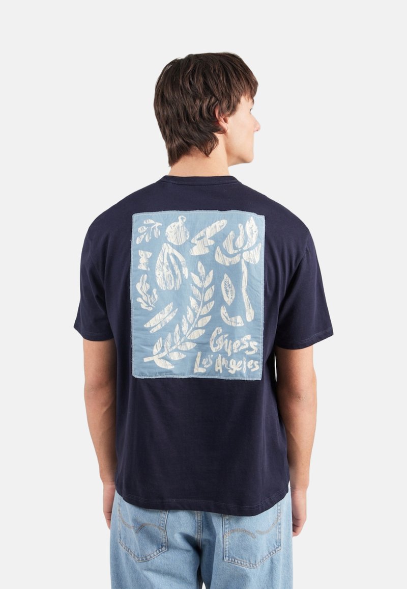 Camiseta de algodón de color azul marino con un gráfico cuadrado de color azul claro en la parte posterior, con formas orgánicas blancas y el texto "Guess Los Angeles".