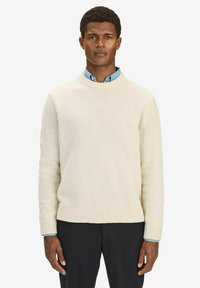 Crèmekleurige wollen sweater met een geribbelde halslijn en zoom. Draagt over een lichtblauwe kraagshirt. Egaal textuur, comfortabele pasvorm.