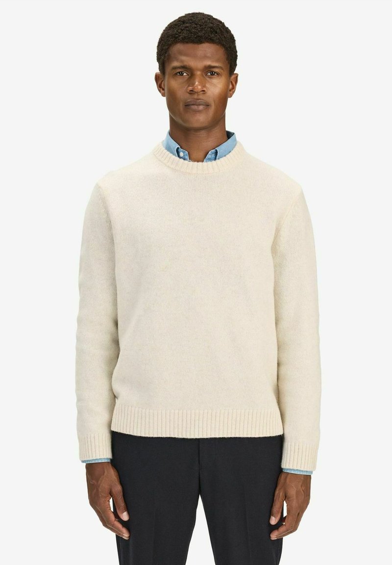 Crèmekleurige wollen sweater met een geribbelde halslijn en zoom. Draagt over een lichtblauwe kraagshirt. Egaal textuur, comfortabele pasvorm.