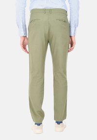 Pantaloni verde oliva con una vestibilità dritta, caratterizzati da due tasche posteriori e una texture liscia. Abbinati a sneaker bianche e un accento blu.