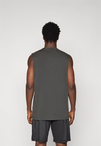 Ermeløs grå treningstopp laget av mykt materiale, med rund hals og løs passform, kombinert med svarte mesh-shorts.