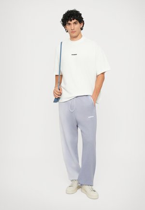 Camisa oversized branca com o logótipo "BONSAI", combinada com calças de moletom azul claras com cintura elástica e logótipo. Ténis neutros.