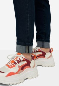 Zapatillas chunky que presentan una mezcla de paneles blancos, rojos y naranjas. Parte superior de malla texturizada, suela gruesa blanca y sistema de cordones tradicional.