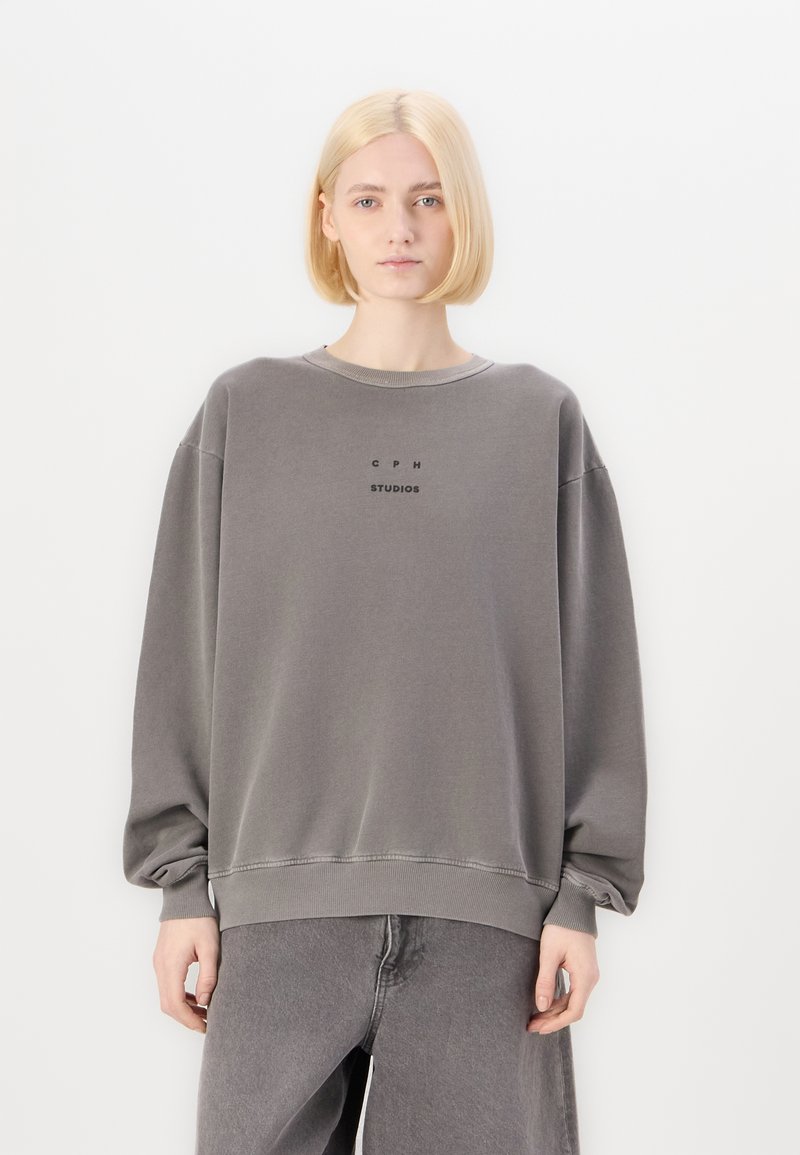 Felpa grigia con collo a giro, vestibilità ampia e spalle scese, caratterizzata da un piccolo logo nero al centro con la scritta "CPH STUDIOS".