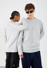 Lys grå langermede gensere med rund hals, parret med svarte og mørkeblå jeans med slitte detaljer.