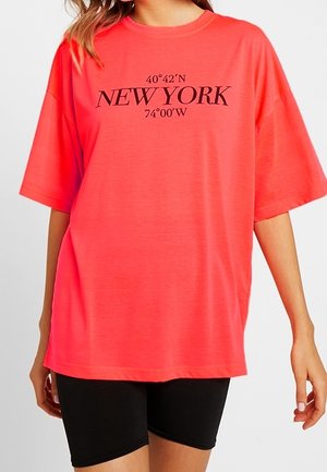 T-shirt oversize fucsia realizzato in materiale leggero, con testo nero "40°42'N NEW YORK 74°00'W" centrato sulla parte anteriore.