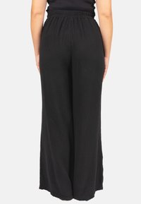Schwarze weitgeschnittene Hose aus strukturiertem Stoff, mit einem elastischen Bund und einer lockeren Passform. Sichtbare Nähedetails auf der Rückseite.