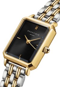 Orologio rettangolare con cassa in acciaio inossidabile dorato, quadrante textured nero, indici delle ore dorati e bracciale in metallo bicolore.