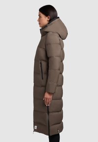 Lång pufferjacka i brunt, med huva, sidofickor och ett quiltat mönster. Materialet ser slätt ut med en lätt glans.