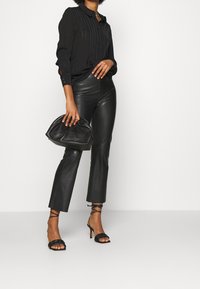 Chemise noire à boutons avec des rayures verticales, associée à un pantalon en cuir noir taille haute. Tenue complétée par un sac à main texturé noir et des talons lanières.